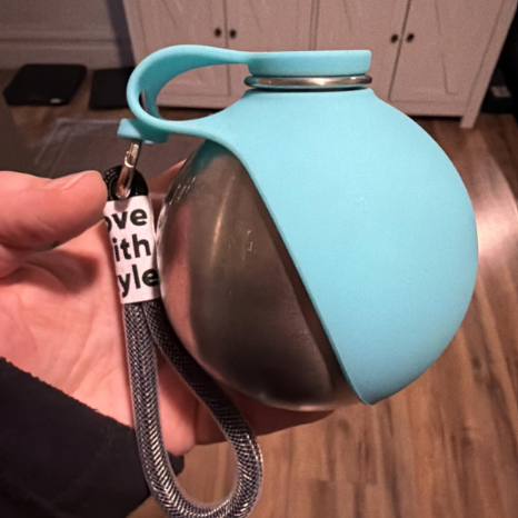 Light blue pet water bottle with a metal spout held by a person indoors.